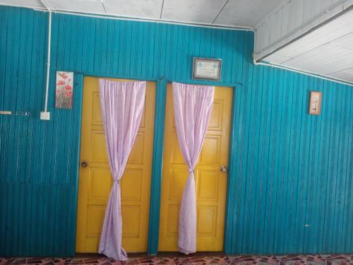 two yellow doors with curtains in a blue wall at Barokah Homestay in Bachok