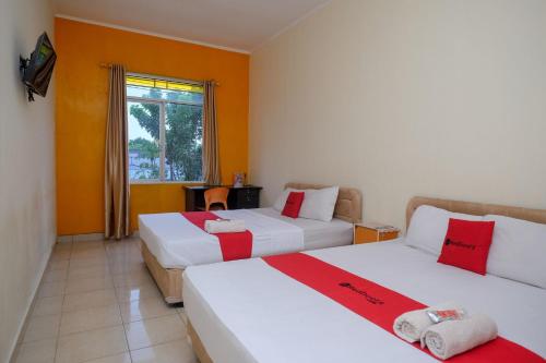 RedDoorz near Jalan Wolter Monginsidi Manado في مانادو: سريرين في غرفة بجدران برتقالية ونافذة