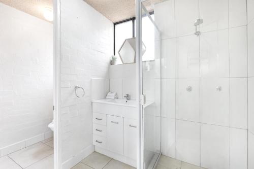 a white bathroom with a shower and a sink at Tindarra Apartments in Alexandra Headland