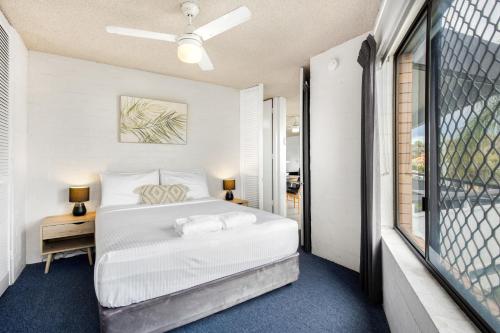 a white bedroom with a bed and a window at Tindarra Apartments in Alexandra Headland