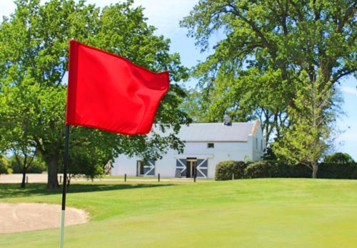 a red flag on a golf course with a white house at Quamby Estate in Hagley