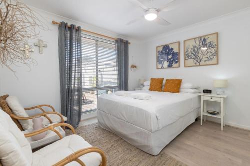 a bedroom with a bed and a chair and a window at The Reef in Boomerang Beach