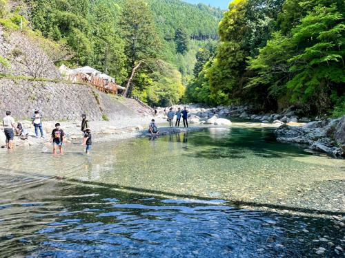 a group of people walking in the water on a river at リバーサイドグランピングNuts in Higashiomi