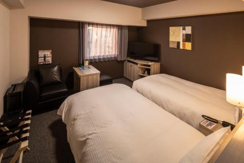 a hotel room with two beds and a chair at Hotel Route Inn Matsuyama -Katsuyama Dori- in Matsuyama