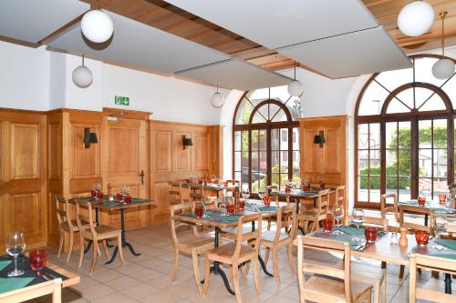 un restaurante con mesas y sillas de madera y ventanas en Hôtel de Ville d'Ollon, en Ollon