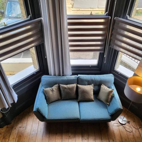 a blue couch with pillows in a room with windows at 21 Mini Loft Apartment - Great Location - Comfy King Size Bed in Brighton & Hove