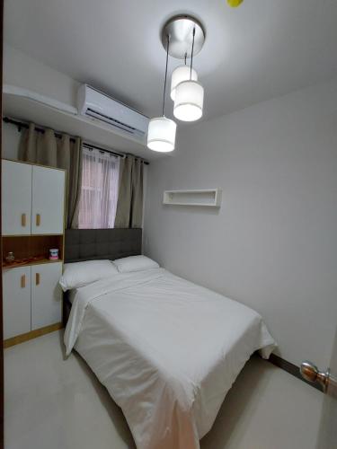 um quarto com uma cama com lençóis brancos e uma luz em Cozy condo at Pasay near MOA Arena em Manila