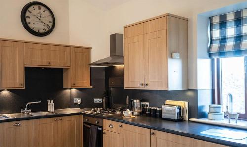 una cocina con armarios de madera y un reloj en la pared en Oak Cottage, Castle Carrock, Nr Carlisle en Castle Carrock