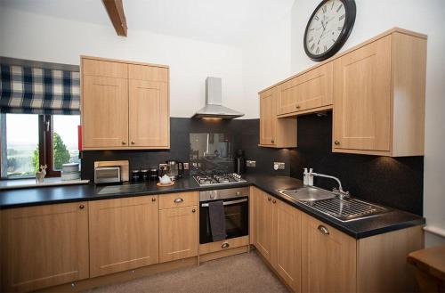 una cocina con armarios de madera y un reloj en la pared en Oak Cottage, Castle Carrock, Nr Carlisle en Castle Carrock