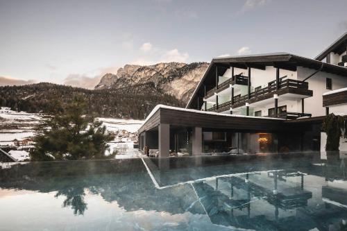 a hotel with a swimming pool in front of a mountain at Biancaneve Family Hotel in Selva di Val Gardena