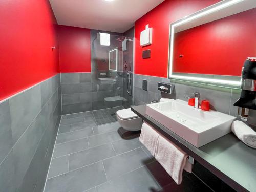 baño con paredes rojas, lavabo y aseo en DORMERO Hotel Hersbruck, en Hersbruck