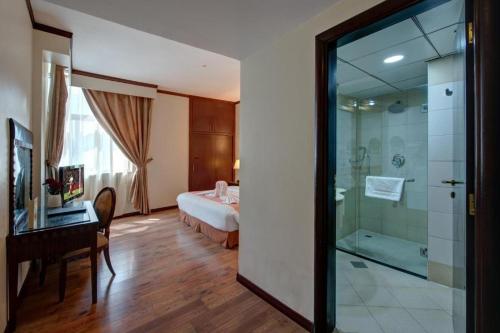 a bathroom with a glass shower and a bedroom at Royal Tulip Apartments in Sharjah