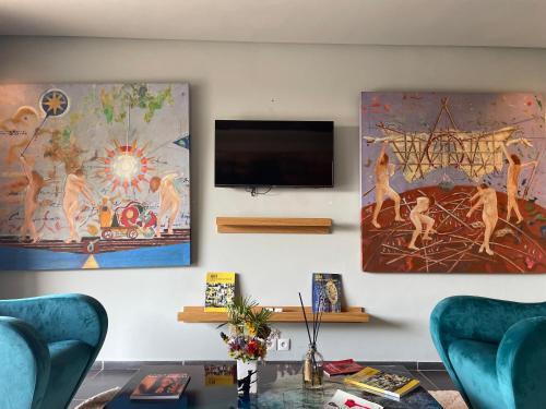 a living room with two blue chairs and a tv on a wall at Kohinor maison d'hôtes in Douar Oulad ben Kheja