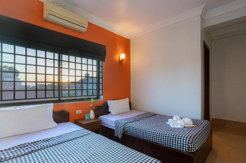 two beds in a room with orange walls and windows at Archaic House in Siem Reap