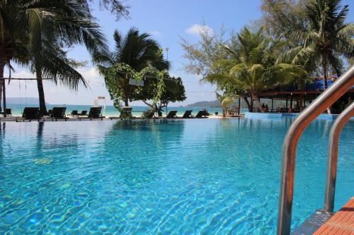 a large swimming pool with palm trees and the ocean at SCARLET SAILS BUNGALOW in Koh Rong Island