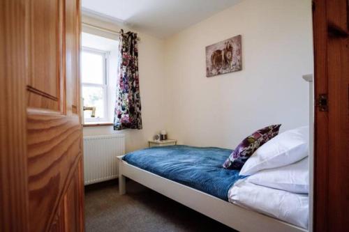 um quarto com uma cama com lençóis azuis e uma janela em Stockman's Cottage em Kirkcudbright