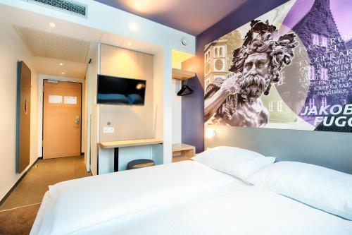 B&B Hotel Augsburg-West في اوغسبورغ: غرفة نوم بسرير ابيض وملصق على الحائط