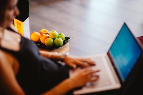 a woman typing on a laptop with a bowl of fruit at Schieners Hotel & Apfelhof Apartments in Wemding