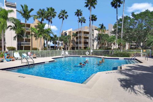 a pool with people in it with palm trees and buildings at Tranquil waterfront condo with pool and steps to beach in Marco Island