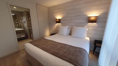 una camera da letto con un grande letto con lenzuola e cuscini bianchi di Logis Hotel La Closerie a La Baule