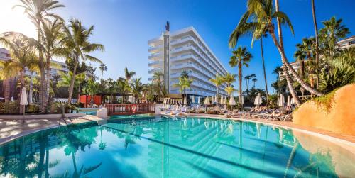 a swimming pool with palm trees and a tall building at Hotel Gran Canaria Princess - Adults Only in Playa del Ingles
