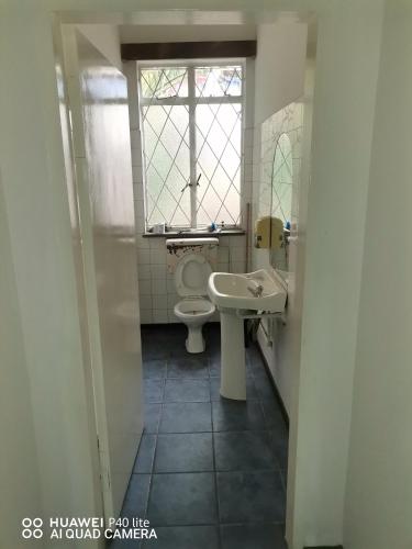 a bathroom with a toilet and a sink and a window at Sunset Executive Lodge in Boksburg