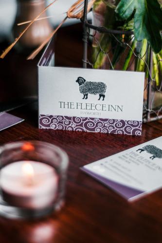 a candle and a sign with a sheep on a table at The Fleece Inn in Haworth
