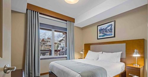 een slaapkamer met een bed en een groot raam bij Mountain View 1 BR Condo With Gym & Hot-Tubs in Canmore