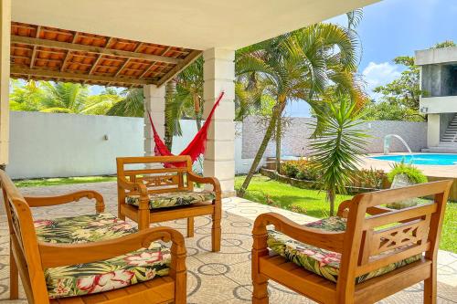 a porch with three wooden chairs and a pool at Casa com piscina em Itacimirim BA in Itacimirim