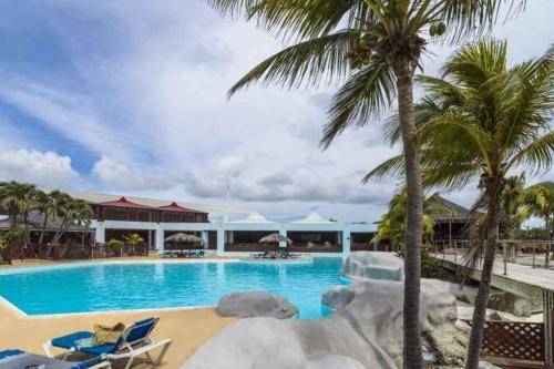 a swimming pool with palm trees and a resort at Studio Kaza Loulou au Manganao Au pied de la plage et piscine in Saint-François