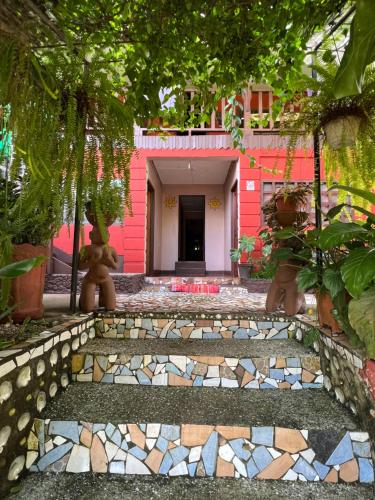 a pathway leading to a pink house with a building at Pura Vida Hostel in Montezuma