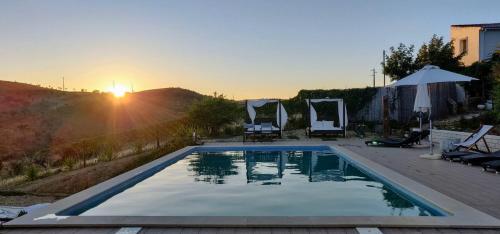 a swimming pool with a sunset in the background at Casas de Campo do Castro da Cola in Marchicão