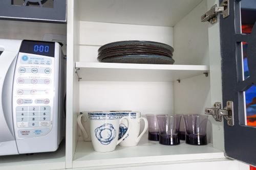 a kitchen pantry with cups and a microwave at Pousada Guaricana in Pontal do Paraná