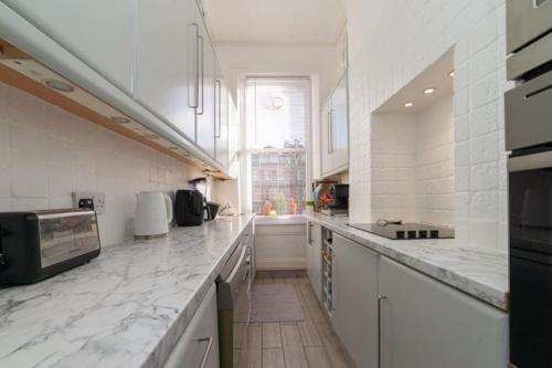 een grote keuken met witte aanrechtbladen en een raam bij Elgin Terrace in Londen