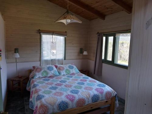 um quarto com uma cama com um edredão e 2 janelas em La casa de la abuela Cabaña em El Bolsón