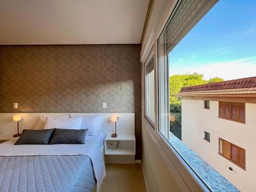 a bedroom with a bed and a large window at Apartamento Villaggio Del Veneto 1 dorm by Achei in Canela