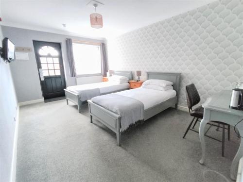 a bedroom with two beds and a table and a desk at Woodcote Hotel in Hooton