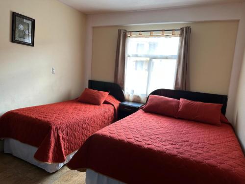 a bedroom with two beds with red sheets and a window at Apartamento #1 Portal de Occidente in Quetzaltenango