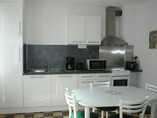 une cuisine avec des armoires blanches et une table avec des chaises dans l'établissement Charmant T2 avec Terrasse Privée, à 600m Plage et Commerces, La Tranche-sur-Mer - FR-1-22-278, à La Tranche-sur-Mer