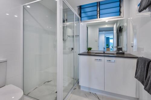 a white bathroom with a shower and a sink at Frangipani Beachfront Lodge F5 on Hamilton Island by HamoRent in Hamilton Island
