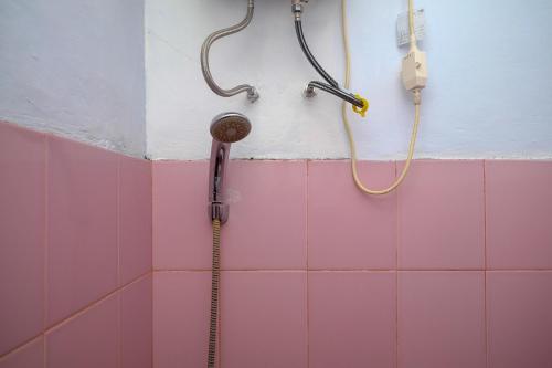 een douche in een badkamer met roze tegels bij RedDoorz at Lapangan Bandara Sam Ratulangi Manado in Manado