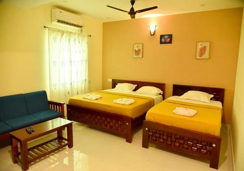 2 Betten in einem Zimmer mit Sofa und Stuhl in der Unterkunft Nilton Bay Residency in Puducherry