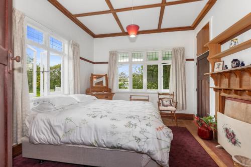 a bedroom with a large bed and windows at Early Settler Homestead - Waipu Holiday Home in Waipu