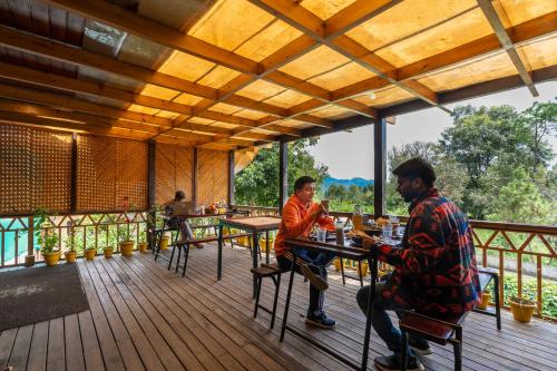two men sitting at tables on the deck of a restaurant at The Hosteller Kasar Devi in Almora