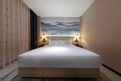 a large white bed in a room with a painting on the wall at Ausotel by Argyle Baiyun International Airport Renhe Metro Exit B in Guangzhou