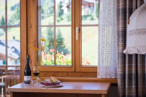 einen Tisch mit einem Teller Essen, einer Flasche Wein und einem Fenster in der Unterkunft Hotel B&B Casa La Val in Sedrun