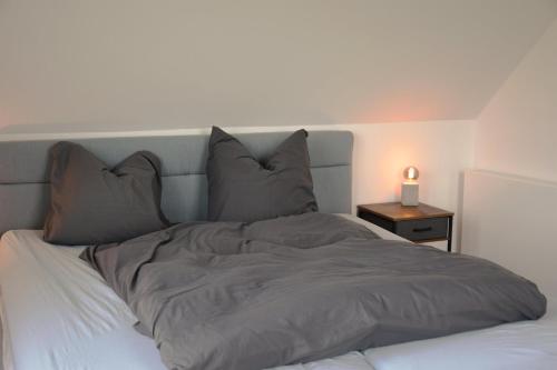 a bed with grey sheets and pillows next to a nightstand at Ferienhaus Reiherweg in Bedekaspel