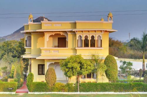 a yellow house with trees in front of it at Padmini Bagh Resort by Inventree, Udaipur in Udaipur