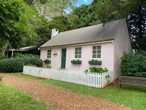une petite maison rose avec une clôture blanche et un banc dans l'établissement Enchanting Retreat - The English Cottage at Tamborine Mountain, à Mount Tamborine