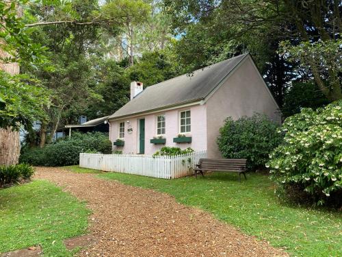 a small white house with a bench in the yard at Enchanting Retreat - The English Cottage at Tamborine Mountain in Mount Tamborine